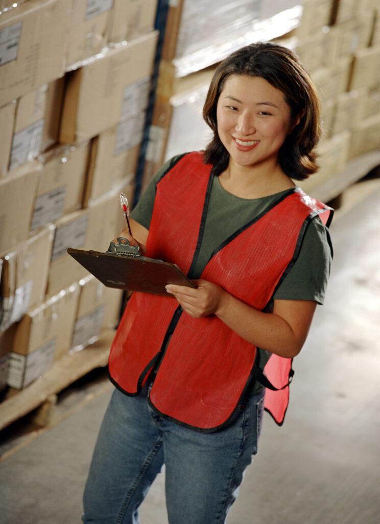 Smiling woman in red safety vest, clipboard.